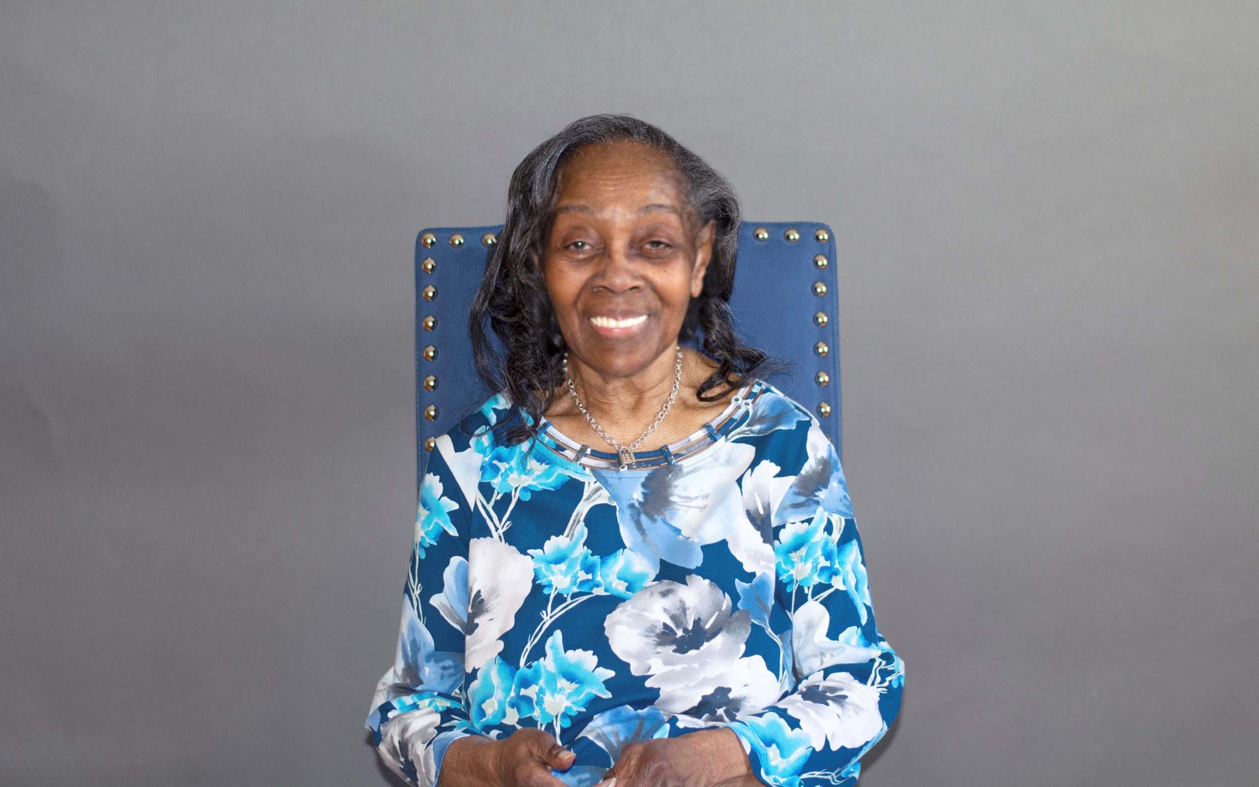 An older woman sitting down in a chair looking at camera smiling