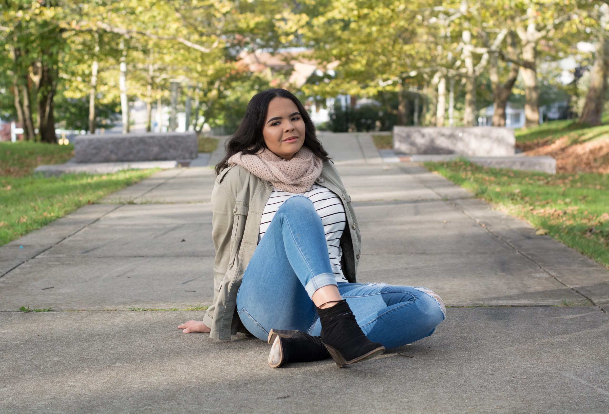 Young lady sitting down on ground with hands behind her and one leg crossed over the other