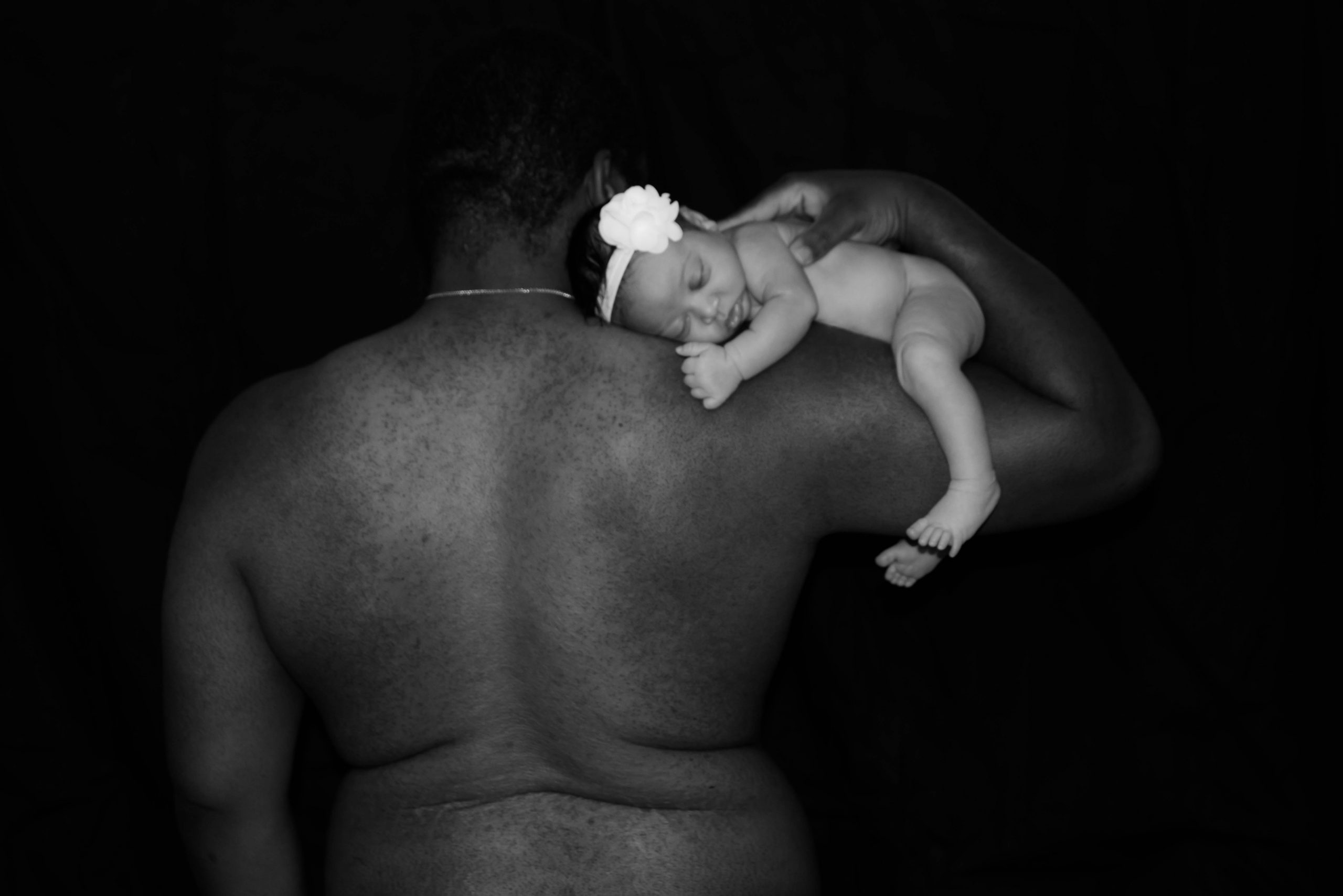 Father flexing his bicep with his newborn daughter laying chest down on it sleeping