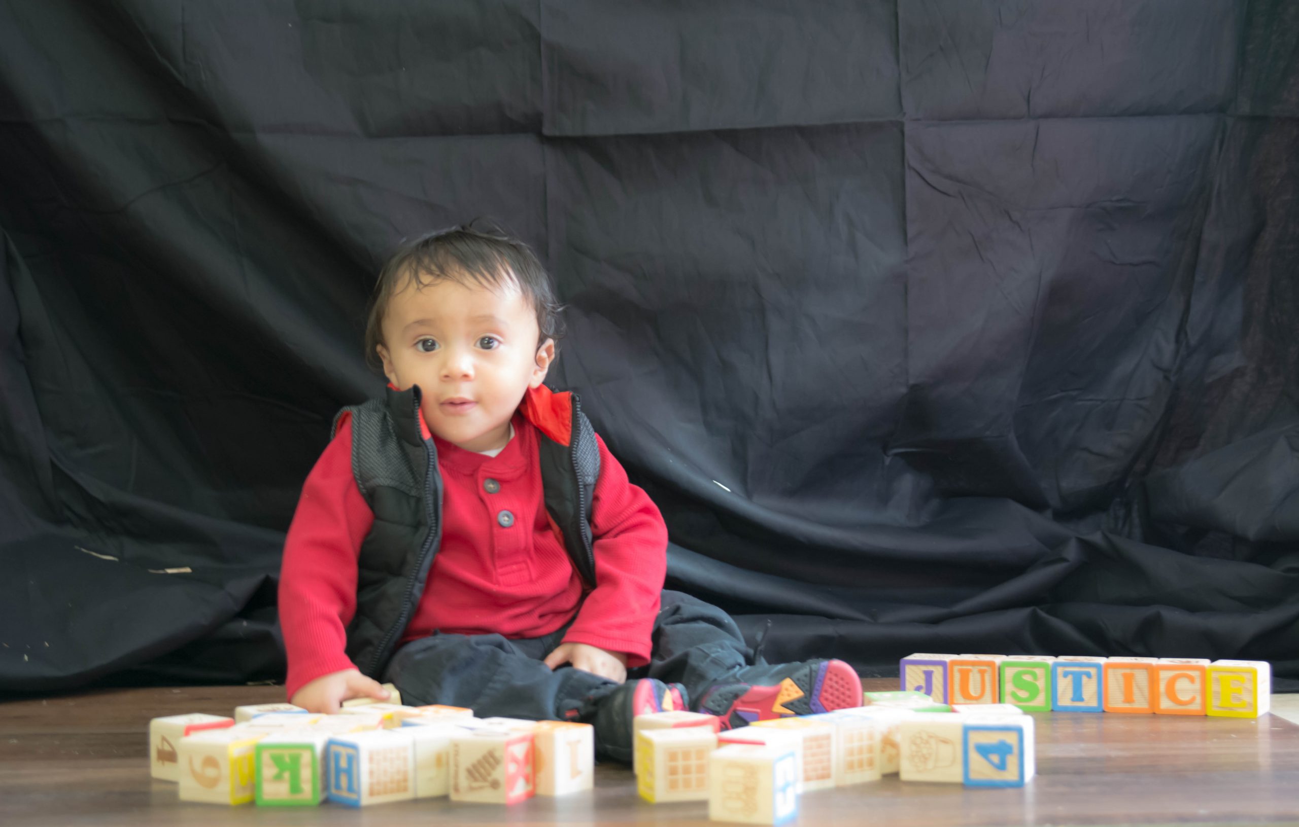 1 year old boy sitting on floor looking at camera surrounded by wooden blocks