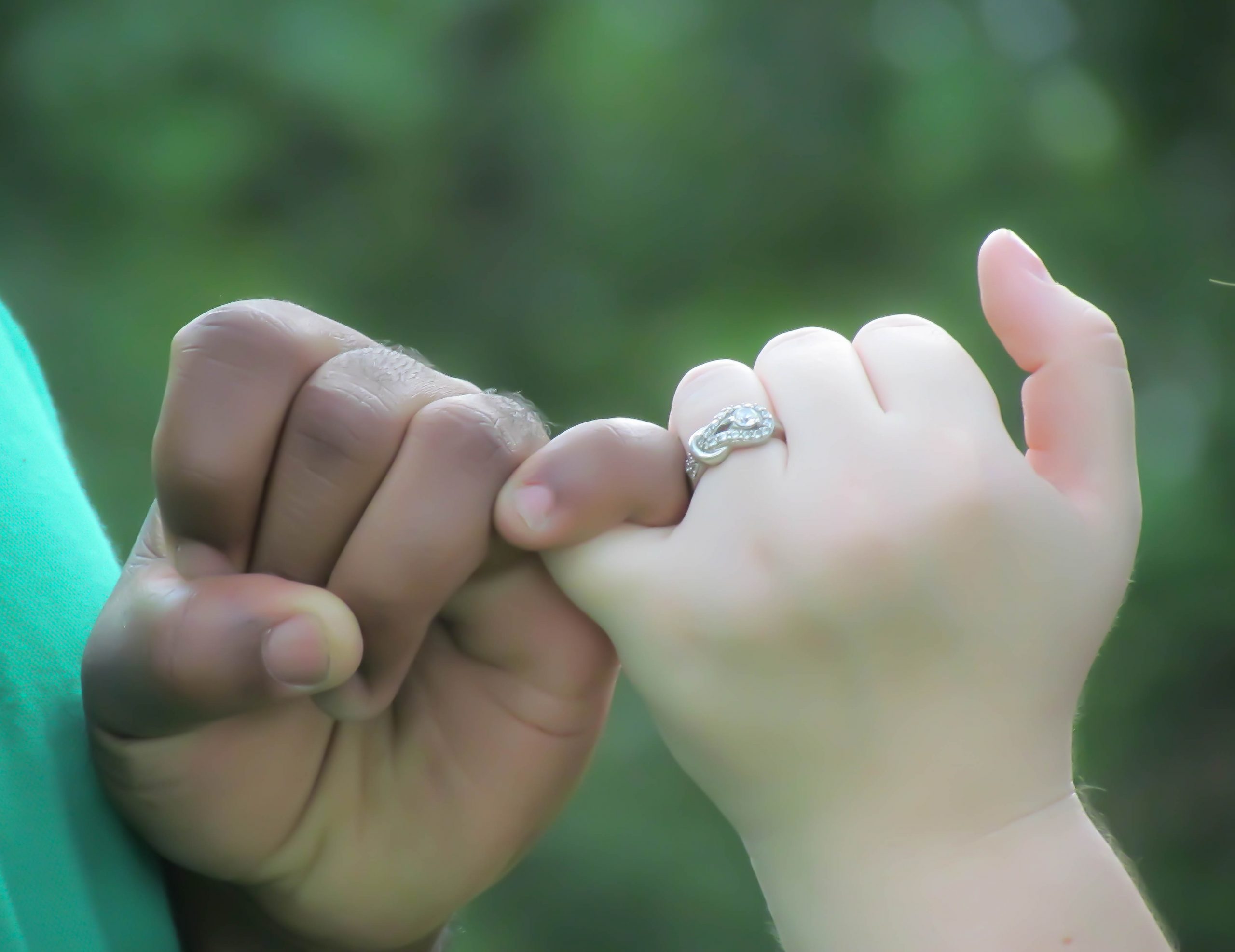 Hands of couple shown doing the pinky promise showing off the engagement ring