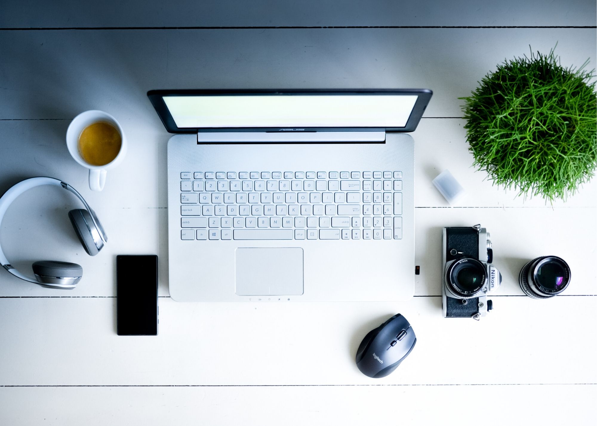 camera, laptop, headphones, cell phone and other items set up neatly on a table